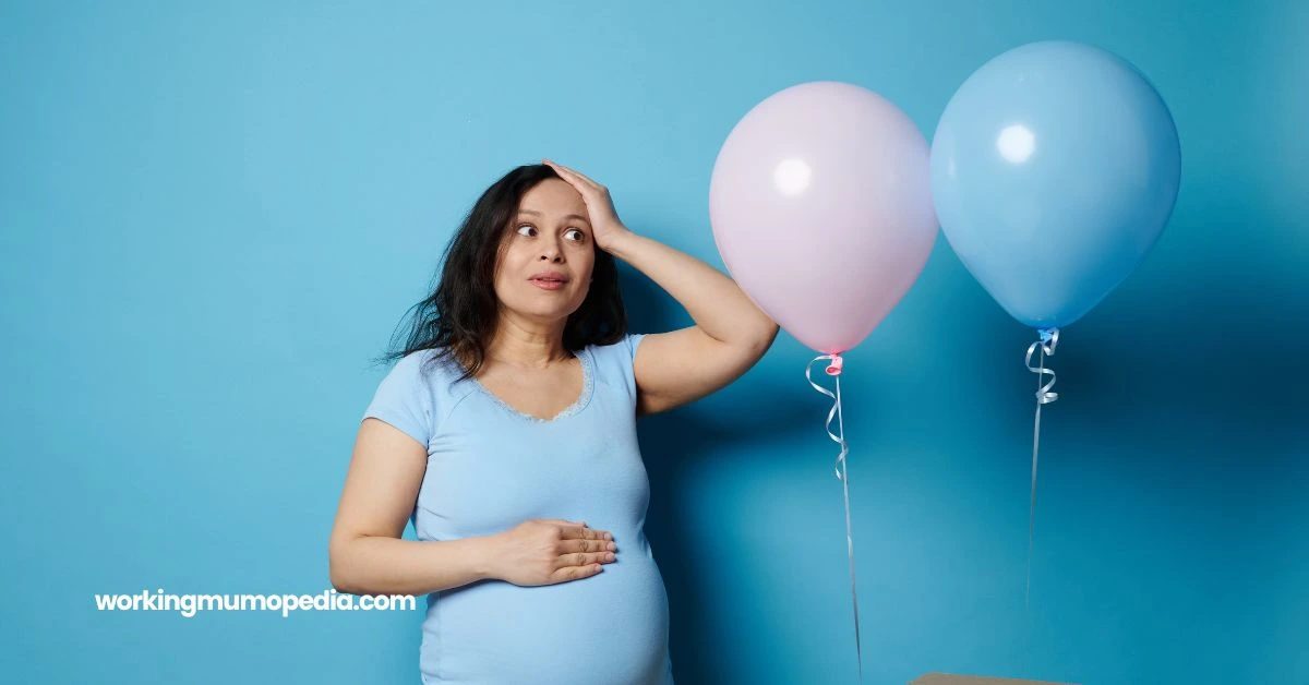Pregnant woman in a light blue shirt standing in front of a blue background, looking thoughtful while holding her baby bump. Two balloons, one pink and one blue, float nearby, symbolizing a gender reveal theme.