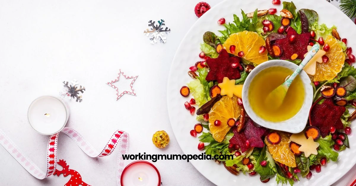 A festive salad featuring sliced oranges, star-shaped beetroot, and pomegranate seeds arranged on a white plate with fresh greens. The plate includes a bowl of golden dressing and a small spoon. The background has Christmas decorations like ribbons, a lit candle, snowflakes, and a star ornament, creating a holiday theme. The text "workingmumopedia.com" is prominently displayed across the image.